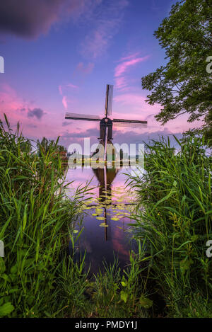 Alte holländische Windmühle und ein Kanal bei Sonnenuntergang in Kinderdijk, Niederlande. Dieses System der 19 Windmühlen wurde um 1740 erbaut und ist heute ein UNESCO Weltkulturerbe. Stockfoto