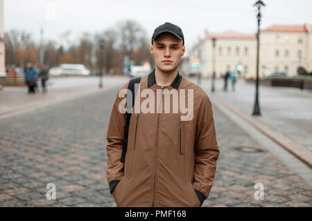 Hübscher junger Kerl in einem fashion Rock mit einer schwarzen Kappe und Tasche Spaziergänge in der Stadt Stockfoto