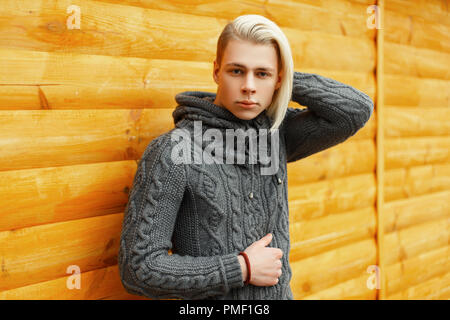Hübscher junger Mann in einem modischen vintage Strickpullover in der Nähe einer Holzwand stellt Stockfoto