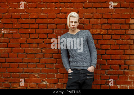 Modische hübscher junger Mann mit einem Haar in einem gestrickten Pullover in der Nähe eines Red brick wall Stockfoto