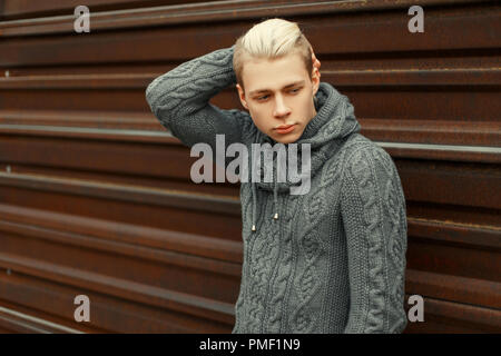 Junger Mann in einem grauen pullover Vintage gestrickt in der Nähe einer Wand aus Metall Stockfoto