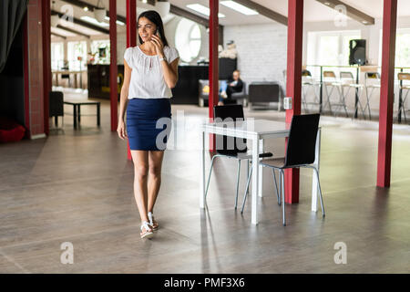 Schöne Frau am Telefon sprechen Wandern im Amt. Portrait von Stilvollen lächelnd Business Woman In modische Kleidung Aufruf auf Handy im Büro Stockfoto