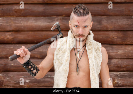 Viking mann Krieger mit einer Axt in der Haut eines Tieres in der Nähe einer Holzwand Stockfoto