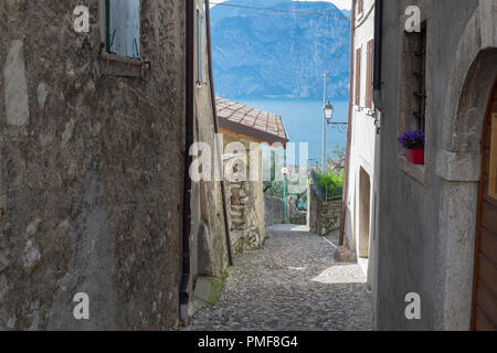 Blick auf den Gardasee mit Berg im Hintergrund von einem alten engen Gang im Dorf Assenza di Brenzone, Bild aus Italien. Stockfoto