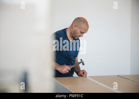 Reifer Mann setzt einen Schrank zusammen in ein neues Zuhause. Stockfoto