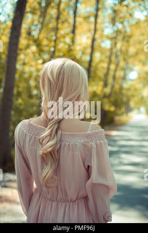 Blonde Frau im rosa Kleid bei Herbst Country Road Stockfoto