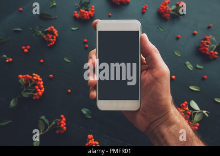 Hand mit Bildschirm des Smartphones mock up auf dunklem Hintergrund mit Blumenschmuck Stockfoto