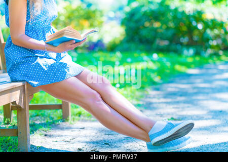 Frau in einem blauen Kleid sitzen auf einer Bank im Stadtpark und ein Buch lesen Stockfoto