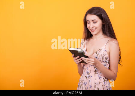 Wunderschöne junge Frau holdin ein Buch im Studio auf gelben Hintergrund. Stockfoto