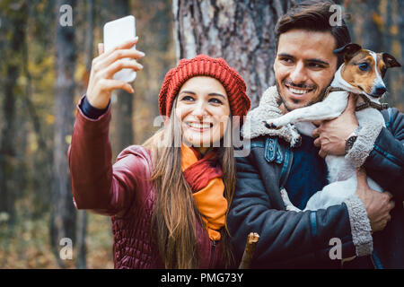 Frau und Mann mit ihren Hund auf Herbst Spaziergang unter einem Telefon selfie Stockfoto