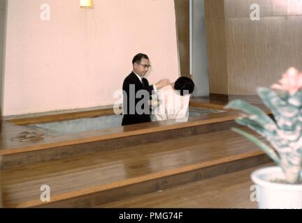 Priester tauft eine japanische Frau, die ihren Kopf Bögen, in einer christlichen missionarischen Kirche in der Nachkriegszeit in Japan, 1965. () Stockfoto