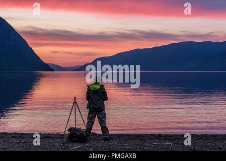 Der Fotograf schaut auf die erstaunliche rosa Sonnenuntergang über den See und die Berge Stockfoto