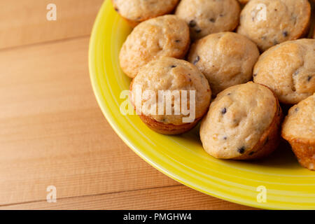 Seite in der Nähe der frisch gebackenen mundgerechte Chocolate Chip Muffins auf gelbem Teller auf einem Holztisch. Stockfoto