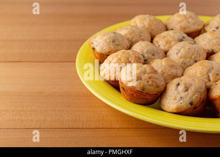 Seitenansicht des frisch gebackenen mundgerechte Chocolate Chip Muffins auf gelbem Teller auf einem Holztisch. Stockfoto