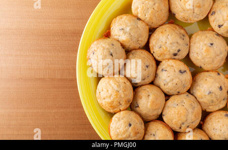 Oben in der Nähe der frisch gebackenen mundgerechte Chocolate Chip Muffins auf gelbem Teller auf einem Holztisch. Stockfoto