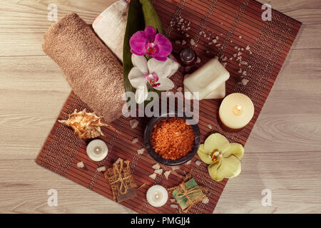 Spa und Wellness Ambiente mit Orchideenblüten, Schüssel mit Meersalz, Seashell, Flasche mit aromatischen Ölen, Seifen, Kerzen und Handtücher auf Bambus Serviette Stockfoto