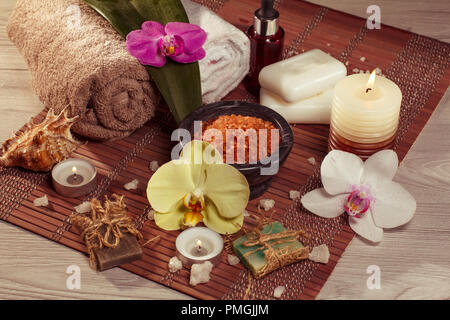 Spa und Wellness Ambiente mit Orchideenblüten, Schüssel mit Meersalz, Seashell, Flasche mit aromatischen Ölen, Seifen, Kerzen und Handtücher auf Bambus Serviette Stockfoto