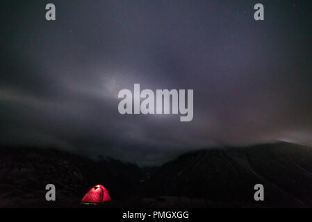 Beleuchtetes Zelt in der Nacht auf den Alpen mit Wolken und Nebel. Camping unter freiem Sternenhimmel, Sommer Abenteuer exploration Fernweh. Stockfoto