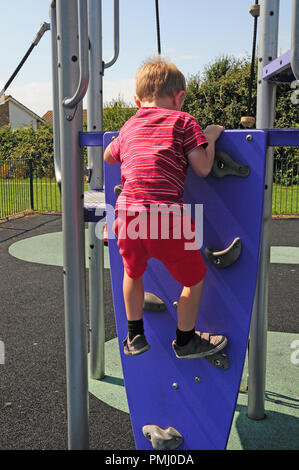 Vier Jahre alten Jungen klettern eine climbling Wand bis zu einer Folie in einen Spielplatz. Stockfoto