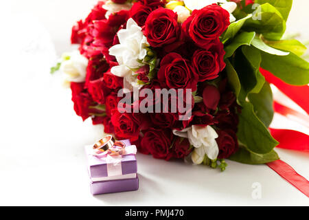 Gold Trauringe auf einem weißen Tisch ist mit einem Strauß Bräute von schönen Blumen. Stockfoto