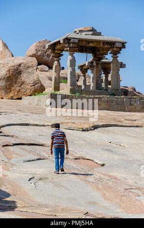 Einsame junge Wandern neben riesige Felsbrocken und Stein Strukturen auf der Hemakuta Hügel bei Hampi, Karnataka, Indien Stockfoto