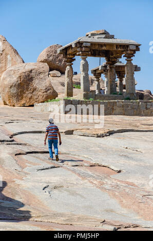 Einsame junge Wandern neben riesige Felsbrocken und Stein Strukturen auf der Hemakuta Hügel bei Hampi, Karnataka, Indien Stockfoto