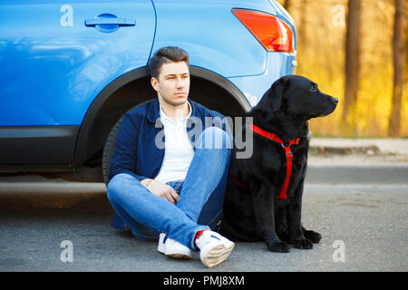 Schöner Mann in modische Kleidung mit einem Hund sitzen in der Nähe des Auto. Genießt zu reisen Stockfoto