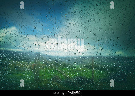 Verschwommen grünen Felder und Wolken über dem Auto Fenster in die Regentropfen fallen. Stockfoto