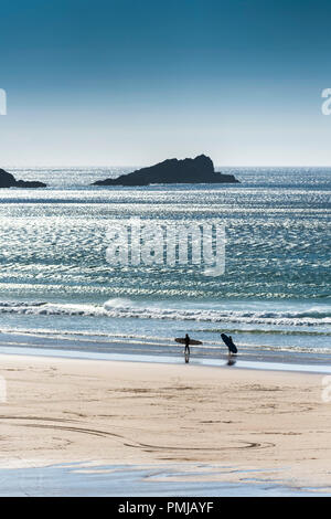 Die Silhouette von zwei Surfer ihre Surfbretter aus dem Meer mit der Gans eine kleine Insel im Hintergrund in Newquay in Cornwall. Stockfoto