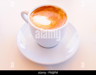 Kleine trinken trinken starken Kaffee mit Milch in eine weiße Keramik Tasse mit Untertasse Stockfoto