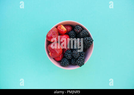 Flach der frisch gepflückte verschiedenen Beeren in eine Schüssel auf blauem Hintergrund. Stockfoto