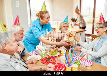 Krankenpflege Hilfe gibt einen Geburtstag zu ein älterer Bürger am Kaffeetisch im Seniorenheim vorhanden Stockfoto