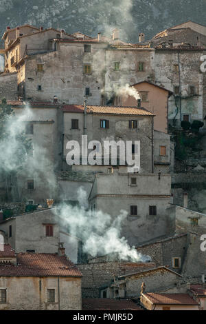 Das kleine und touristische Dorf Ortona dei Marsi wird von dem ersten Winterlicht mit dem Rauch beleuchtet, der aus den Kaminen der Häuser kommt. Abruzzen Stockfoto