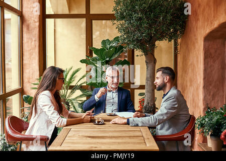 Business Lunch. Drei Leute im Restaurant am Tisch sitzen, trinken heißen Kaffee diskutieren Projekt Freude. Team Konzept Stockfoto