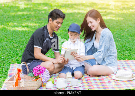 Asian teen Familie lehre Sohn Hausaufgaben beim Picknick im Freien Park Stockfoto