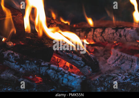 Verkohltes Holz im Feuer. Das Verbrennen von Holz in hellen Flammen im Dunkeln, bis zu schließen. Dunkel getönten Feuer Hintergrund. Stockfoto