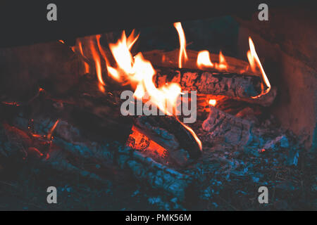 Verkohltes Holz im Feuer. Das Verbrennen von Holz in hellen Flammen im Dunkeln, bis zu schließen. Dunkel getönten Feuer Hintergrund. Stockfoto