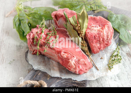 Teilstücke von Rindfleisch für das Grillen auf einem hölzernen Schneidebrett mit Spinat, Rosmarin und Kräutern der Provence für die Marinade in einer rustikalen Stil. Stockfoto