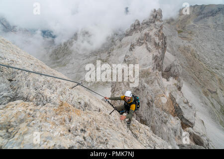 Jungen gutaussehenden männlichen Studenten auf einem steilen und exponierten Fels klettert ein Klettersteig in Alta Badia in Südtirol Stockfoto