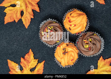 Ahorn Blätter und Halloween Cupcakes auf schwarzem Hintergrund Stockfoto