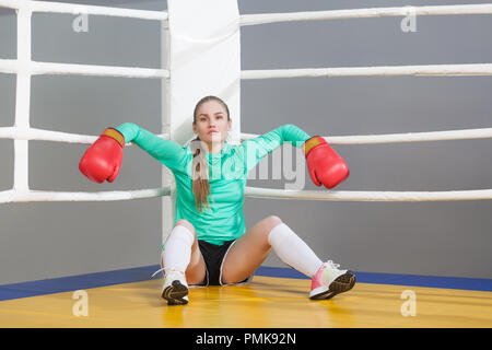 Portrait von zuversichtlich, schöne junge Athlet Frau mit gesammelten Haare Standortwahl und lehnte sich in der Ecke der Boxring in roten Handschuhe und c Stockfoto