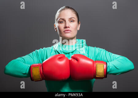 Ernsthafte zuversichtlich, schöne junge Athlet Frau mit gesammelten Haare stehen in der Position in der oberen Arme, Hände zusammen im Boxen rote Handschuhe. Stockfoto