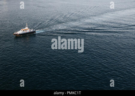 Ein Pilot Boot begleiten ein großes Kreuzfahrtschiff (nicht im Bild) aus dem Anschluss. Vor dem Hintergrund des Meeres isoliert. Stockfoto