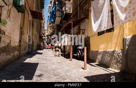 Mann sitzt vor dem Haus in einer alten Gasse in der Mitte der Stadt, Neapel, Italien, Europa Stockfoto