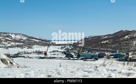 Ein Blick auf den gefrorenen Schnee und Eis bedeckte Bucht mit Schiffen und Produktionsgebäuden vor dem Hintergrund der winter hügel in Petropawlowsk-kamtschatski Stockfoto