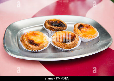 Vier traditionelle Portugiesische pasteis de Natas (Pudding) auf einem silbernen Tablett auf einem rosa und rot gestreiften Tabelle Stockfoto