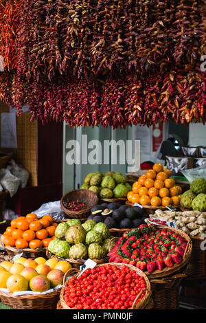 Tropische Frucht in traditionellen Körbe angezeigt und hängende rote Chilis auf einem Marktstand in Mercado dos Lavradores in Funchal. Stockfoto