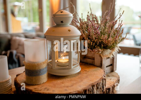 Weiße Laterne mit Kerze drin stehen auf festlichen Tisch auf Holz schneiden und Blumen auf Hintergrund eingerichtet. Dekor. Hochzeit. Herbst noch leben. Getönten Bild. Pink Heather Stockfoto