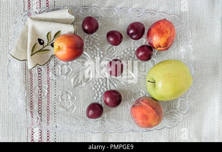 Auf dem Tisch ein Bettwäsche serviette Glas, auf dem liegen, Pflaumen, Äpfel, Pfirsiche. Stockfoto