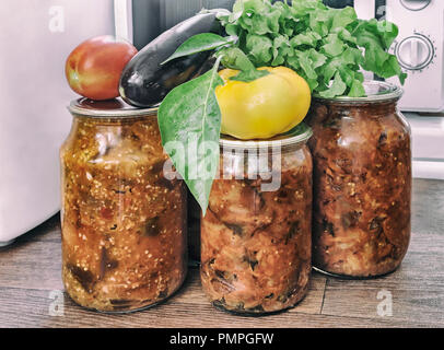 Verschiedene Gemüse in Gläsern mit abgedichteten Metallgehäuse mit Deckel: Auberginen, Paprika, Tomaten, Zwiebeln bewahrt. Frisches Gemüse und Salat sind in der Nähe von Stockfoto